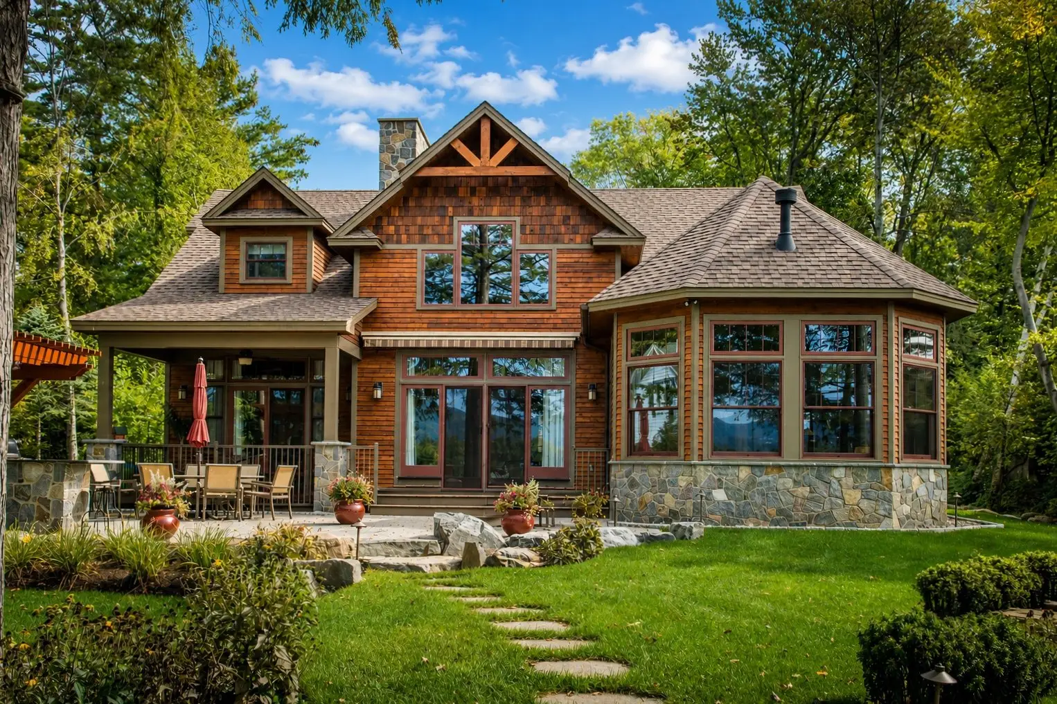 Cedar and stone home with a timber gable and a patio overlooking the lake