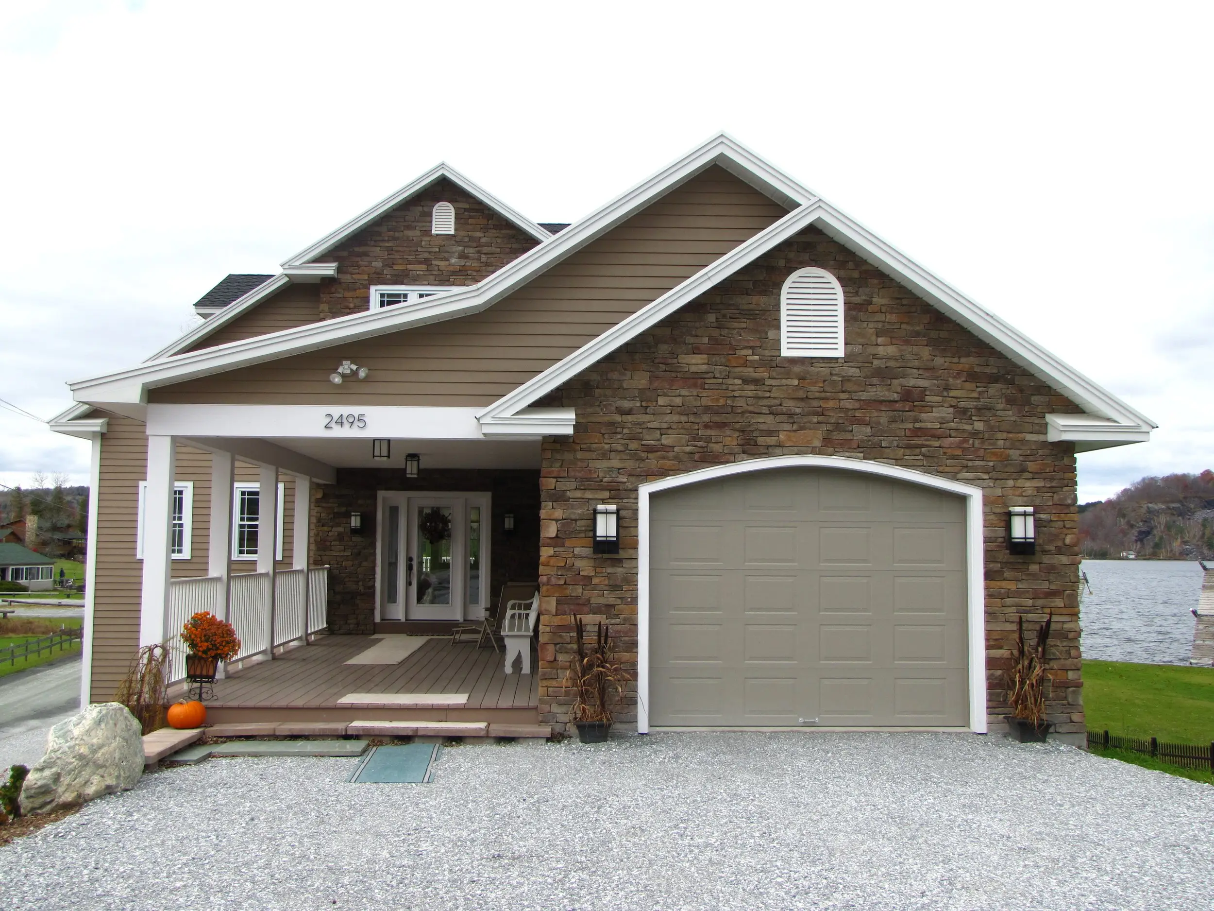 Stone and tan-sided home with a covered entry and a single garage by the water
