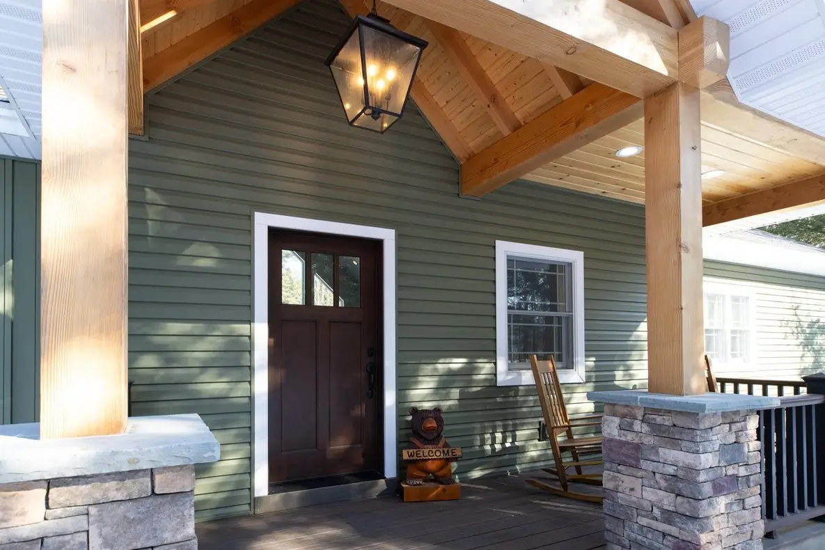 Green-sided porch with timber posts, stone column bases and a dark wood door