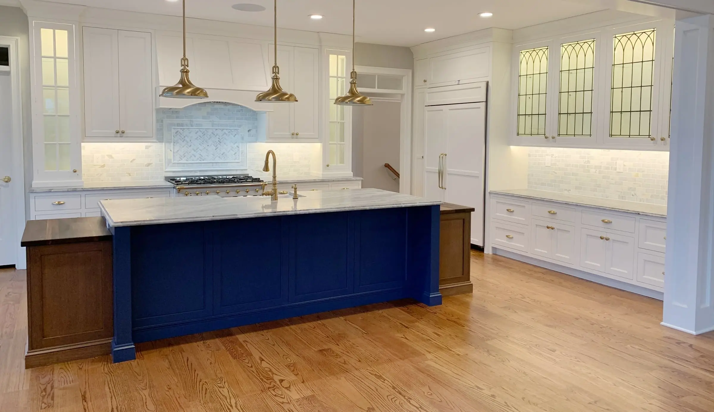 Kitchen with a navy island, brass pendants and leaded-glass cabinets